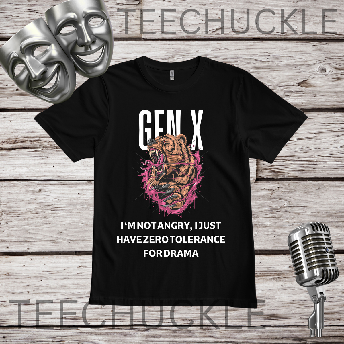 A black graphic t-shirt featuring a roaring bear illustration with pink paint splatters and the text 'GEN-X I'M NOT ANGRY, I JUST HAVE ZERO TOLERANCE FOR DRAMA'. The t-shirt is displayed on a rustic wood background with silver theater masks, a vintage microphone