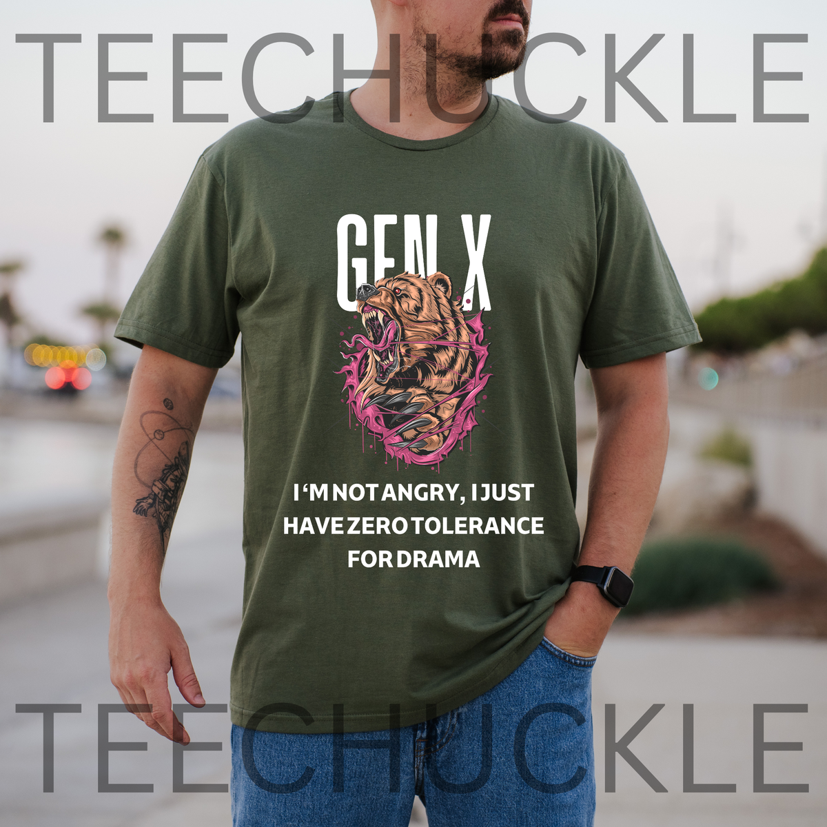 A man wearing a green graphic t-shirt with a roaring bear illustration and the text 'GEN X I'M NOT ANGRY, I JUST HAVE ZERO TOLERANCE FOR DRAMA'.  The background is a blurred outdoor street scene.
