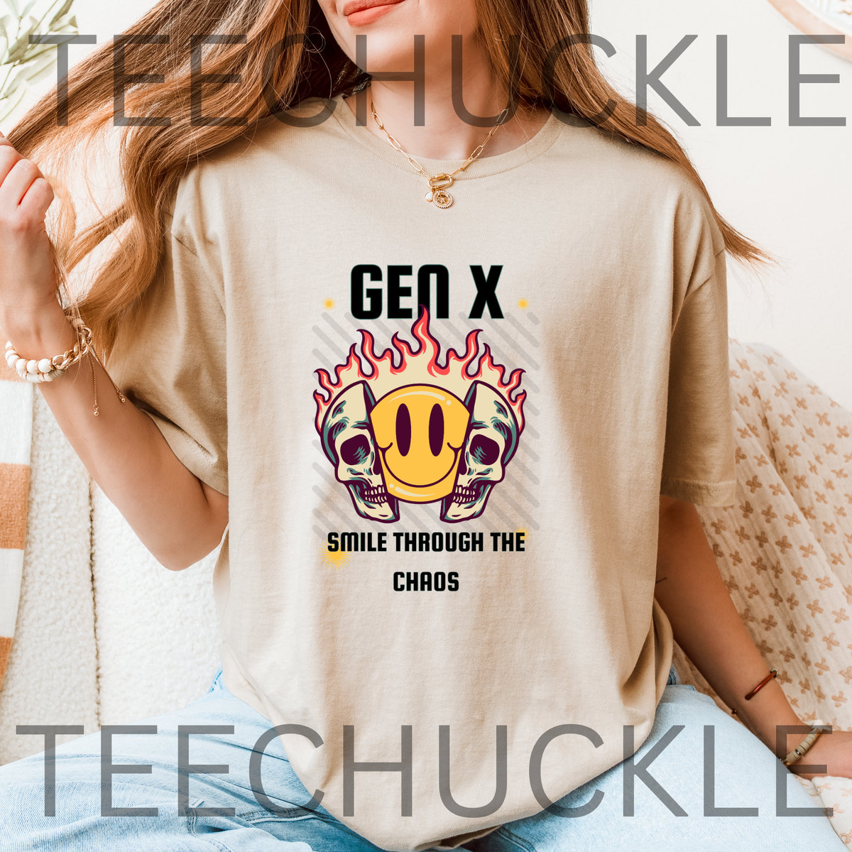 A woman wearing a sand graphic t-shirt with a 'Gen X Smile Through The Chaos' design featuring skulls and a smiley face with pause button, set against a cozy indoor background