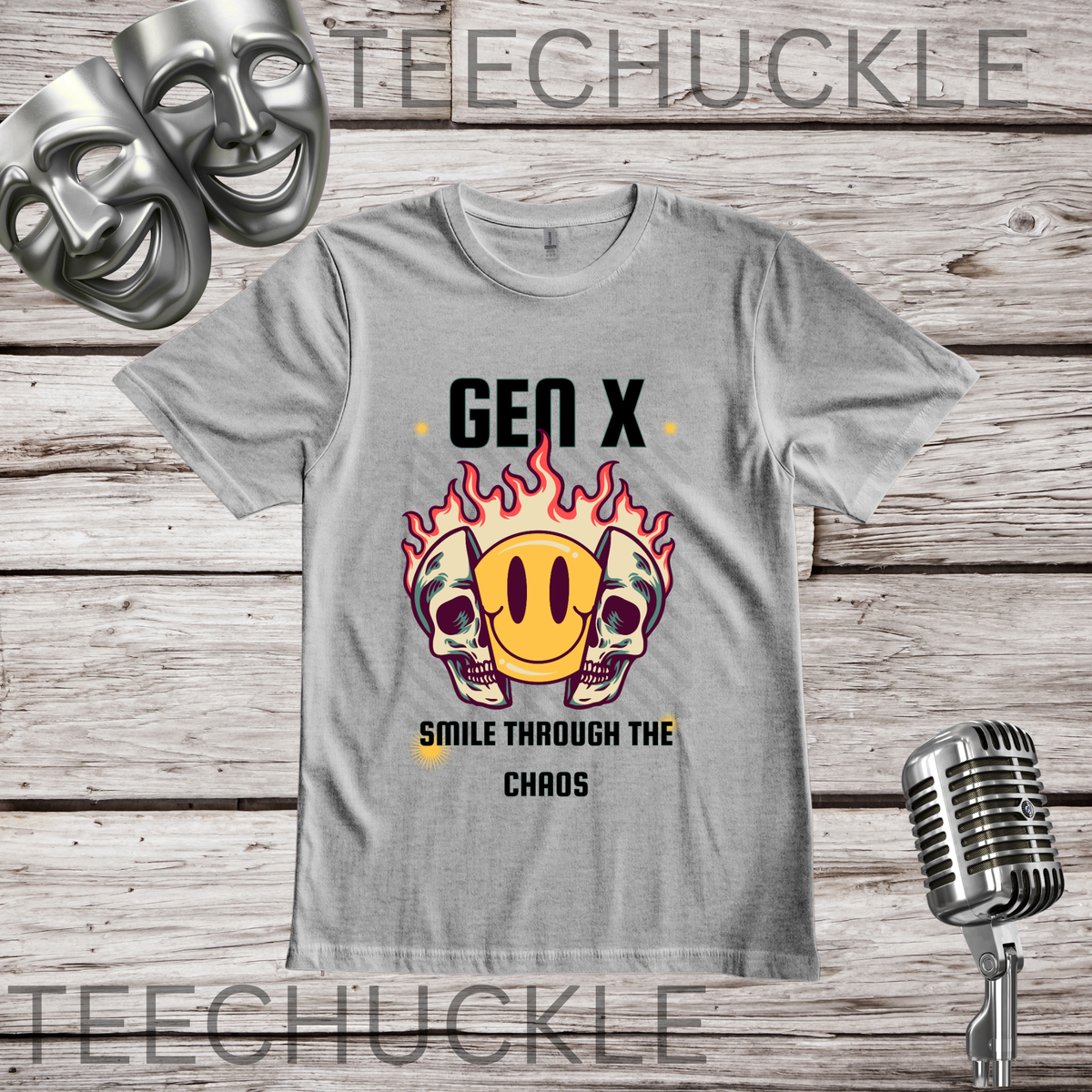 A gray graphic t-shirt displayed on a rustic wood background, featuring a 'Gen X' emoji-themed skull and flame design. The t-shirt is styled with vintage props including a silver microphone and theatrical comedy masks