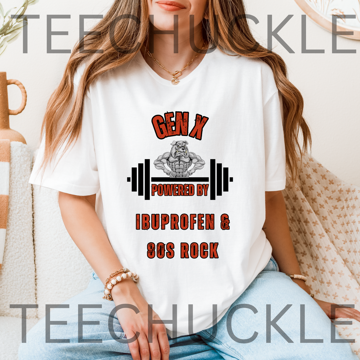 A woman sitting wearing a white graphic t-shirt. The shirt has a bulldog with a barbel graphic and the text 'GEN X POWERED BY IBUPROFEN & 80S ROCK'. 