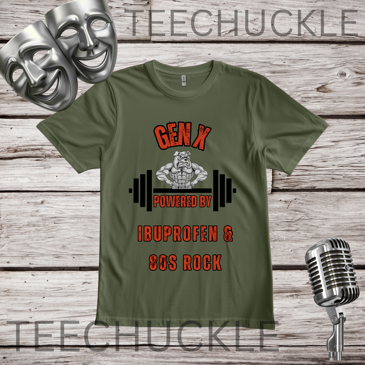 A green graphic t-shirt displayed on a rustic wood background, featuring a design with two silver comedy masks, a vintage microphone, and the text 'GEN X POWERED BY IBUPROFEN & 80S ROCK' with a muscular bulldog cartoon character and barbell graphic. 