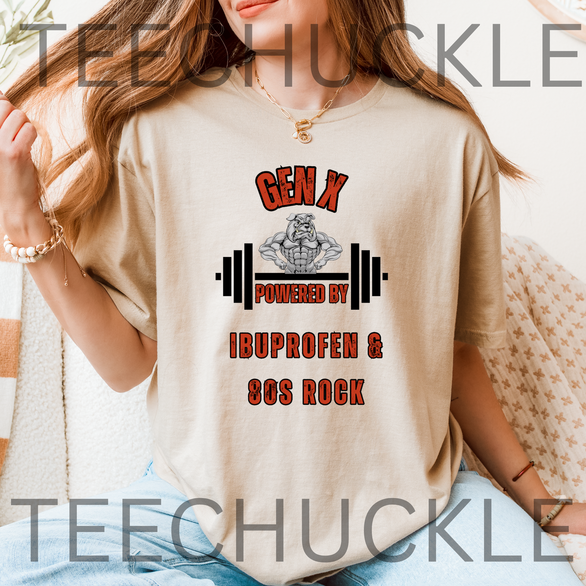 A woman wearing a sand graphic t-shirt with a 'Gen X Powered by Ibuprofen & 80s Rock' design, sitting in a cozy indoor setting.
