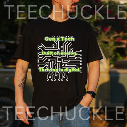 A man wearing a black graphic t-shirt with a white circuit board design and green text reading 'Gen X Tech Built on analog Thriving in digital.' The background is an outdoor blurred setting with a car and foliage