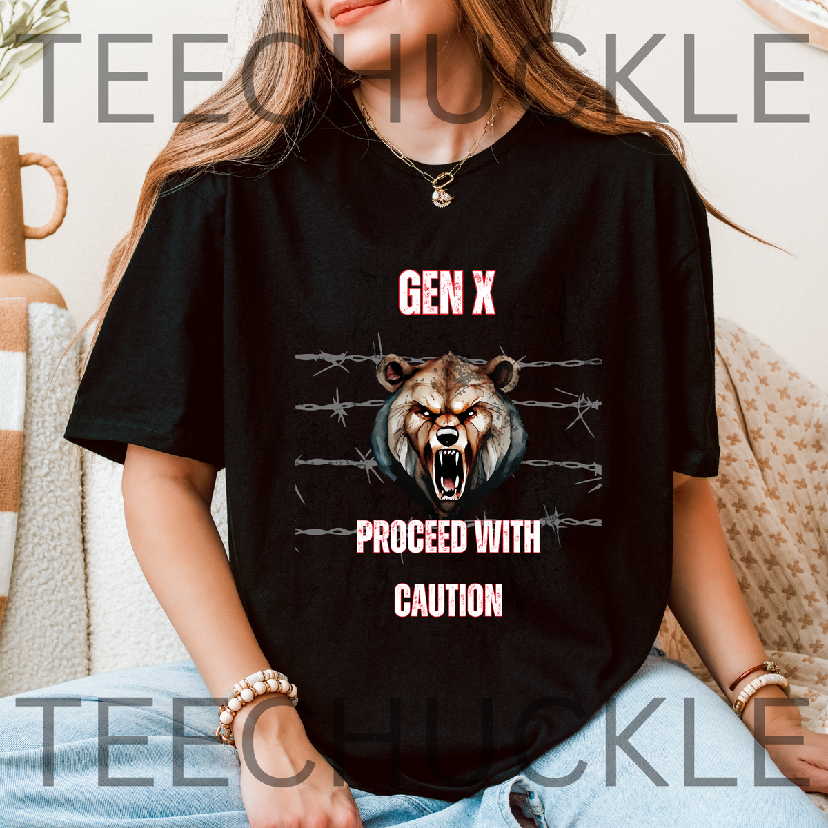 A woman sat on a coch wearing a black graphic t-shirt featuring a roaring bear illustration and the text 'GEN X PROCEED WITH CAUTION'. 