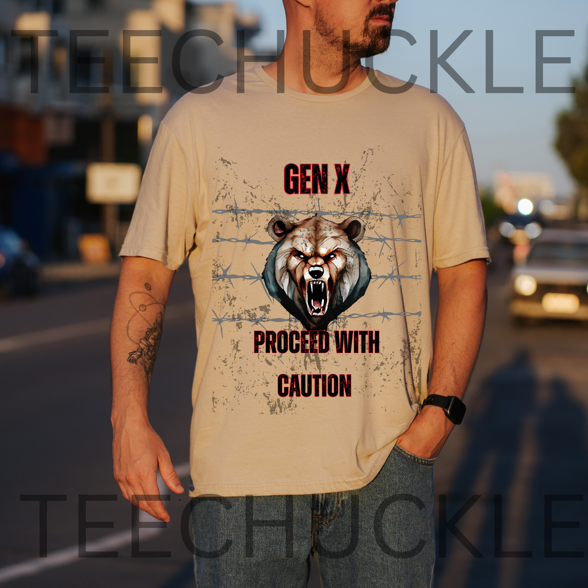 A man wearing a sand graphic t-shirt with a roaring bear design and the text 'GEN X PROCEED WITH CAUTION'. The background is a blurred street scene at sunset.