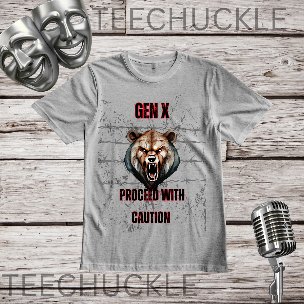 A gray graphic t-shirt featuring a roaring bear head and the text 'GEN X PROCEED WITH CAUTION' in red and black, displayed on a rustic wood plank background with a vintage microphone and comedy masks.