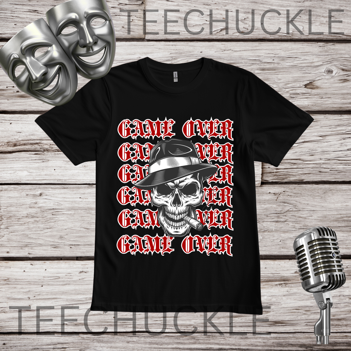 A black short-sleeve graphic T-shirt laid flat on a wood plank background, featuring a skull in a hat smoking a cigerette design with the text 'GAME OVER' repeatedly stacked. Decorative vintage microphones and a microphone and comedy masks appear at the top left and bottom right.