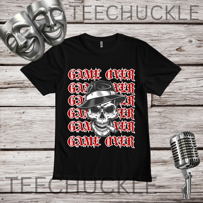 A black short-sleeve graphic T-shirt laid flat on a wood plank background, featuring a skull in a hat smoking a cigerette design with the text 'GAME OVER' repeatedly stacked. Decorative vintage microphones and a microphone and comedy masks appear at the top left and bottom right.