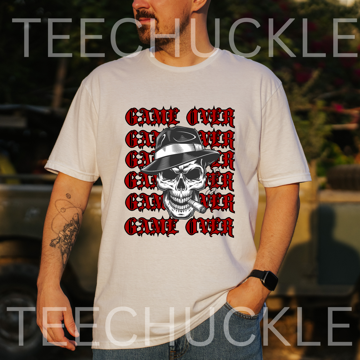 A man wearing a white graphic t-shirt with a 'Game Over' skull design in red and black, set against an outdoor blurred background