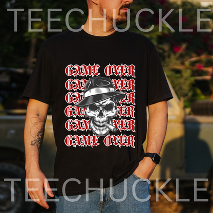 A man wearing a black graphic t-shirt with a repeating 'GAME OVER' text design in red and white around a central skull wearing a hat and smoking a cigar. The background is an outdoor blurred setting with a car.