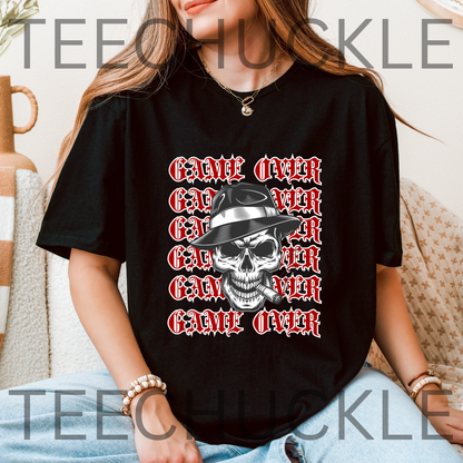 A black short-sleeve graphic T-shirt laid flat on a wood plank background, featuring a skull in a hat smoking a cigerette design with the text 'GAME OVER' repeatedly stacked.
