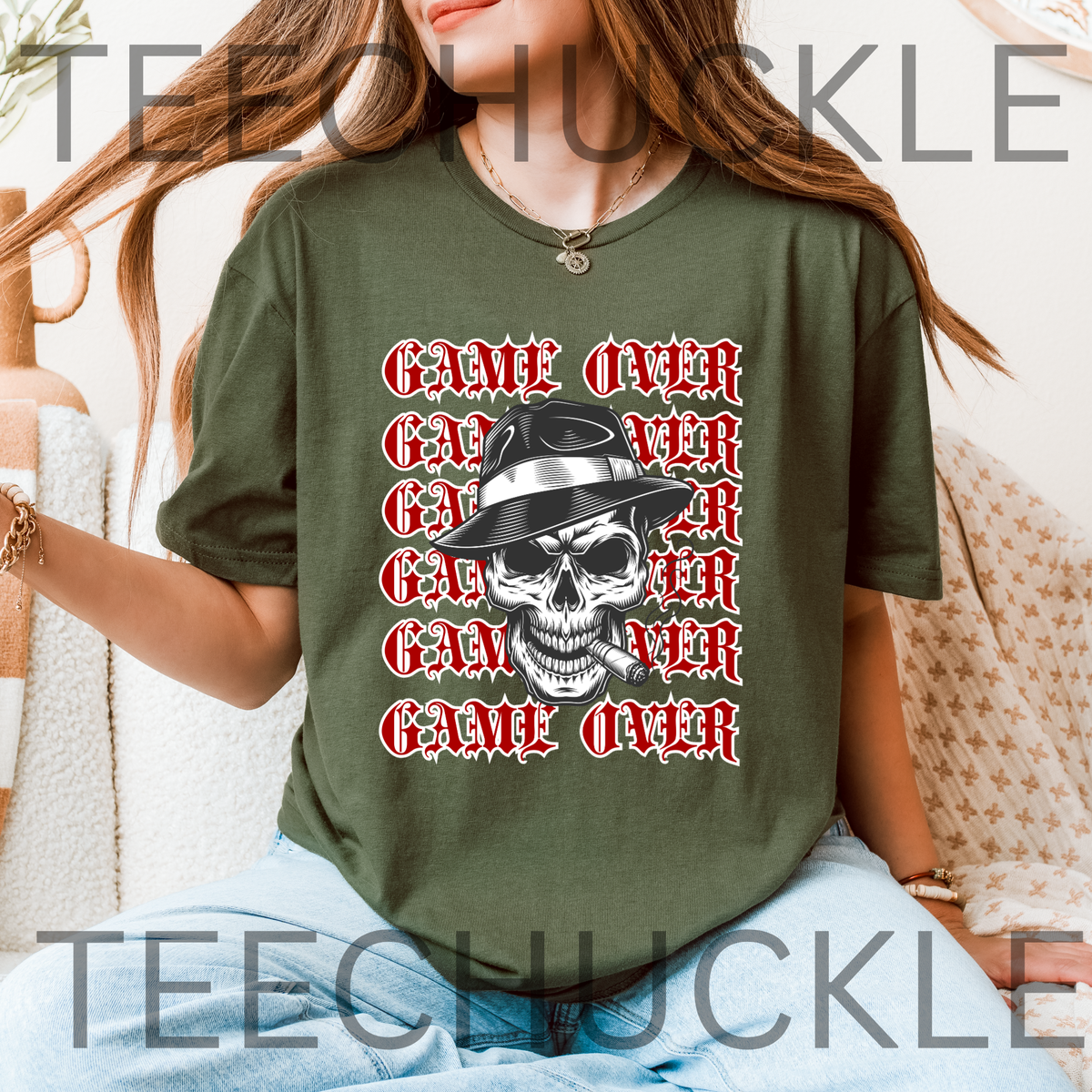 A woman wearing a green graphic t-shirt with a repeating red and white 'GAME OVER' text design and a central skull wearing a black and white fedora hat. 
