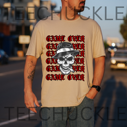 A man wearing a sand graphic t-shirt with a repeating red and black 'GAMEN OVER' design and a skull wearing a hat. The background is a blurred street scene at sunset