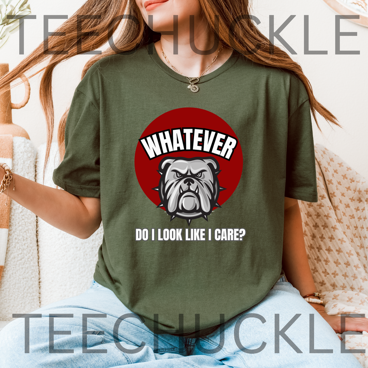 A woman wearing a green graphic t-shirt with a red circular bulldog design and the text 'WHATEVER DO I LOOK LIKE I CARE?' on the front, set against a cozy indoor background.
