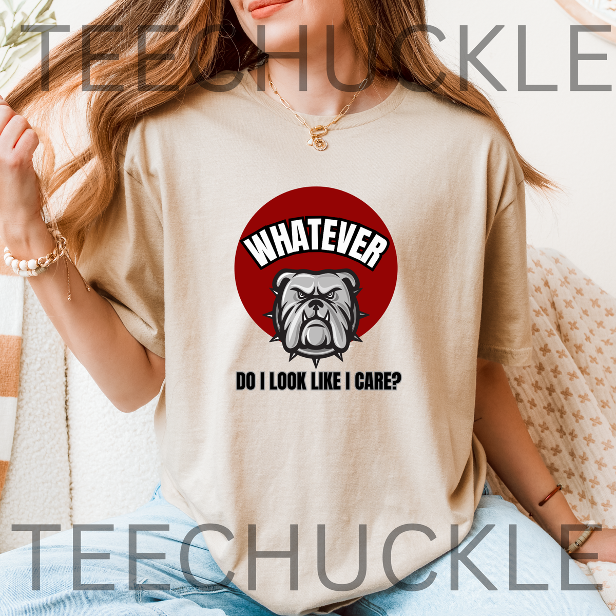 A woman in an indoor setting wearing a sand t-shirt  The shirt has a red circle with a bulldog on it and the text that reads " WHATEVER, DO I LOOK LIKE I CARE"