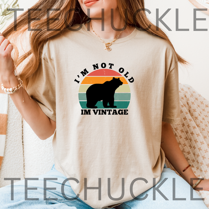 A woman wearing a beige graphic t-shirt with a retro bear design and the text 'I'M NOT OLD IM VINTAGE'.