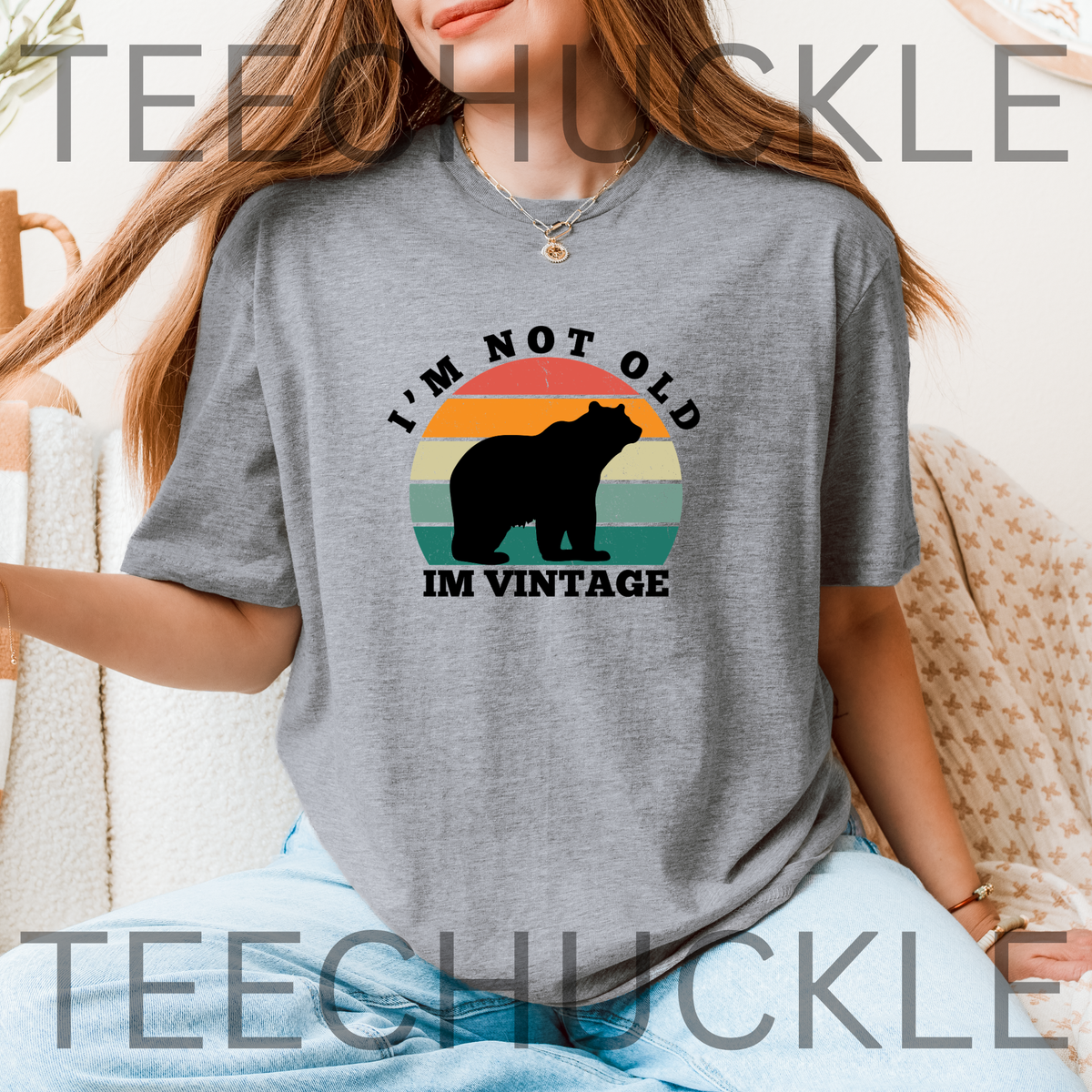 A woman wearing a gray graphic t-shirt with a retro sunset design and a black bear silhouette. The text reads 'I'M NOT OLD' above the sunset and 'IM VINTAGE' below.