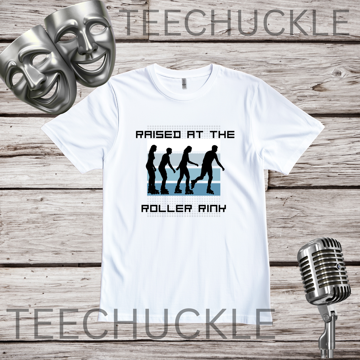 A white graphic t-shirt displayed on a rustic wood background, featuring a black and blue roller rink design with the text 'RAISED AT THE ROLLER RINK'. Two silver comedy masks and a vintage microphone are styled as prop.
