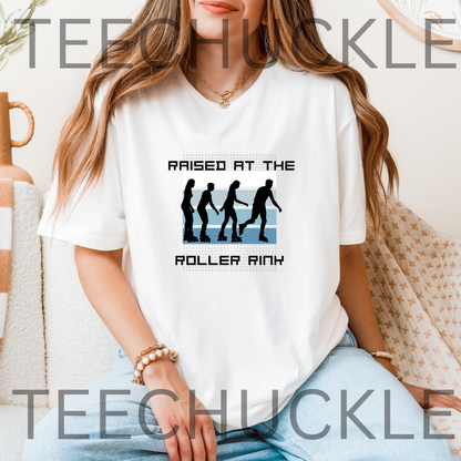A woman wearing a white graphic T-shirt with the text 'RAISED AT THE ROLLER RINk' and a black-and-blue roller rink silhouette design, seated indoors