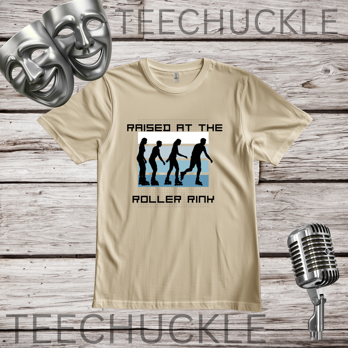 A sand graphic t-shirt displayed on a rustic wood background, featuring a roller rink silhouette design with the text 'RAISED AT THE ROLLER RIN'. The shirt is styled with silver comedy and microphone props