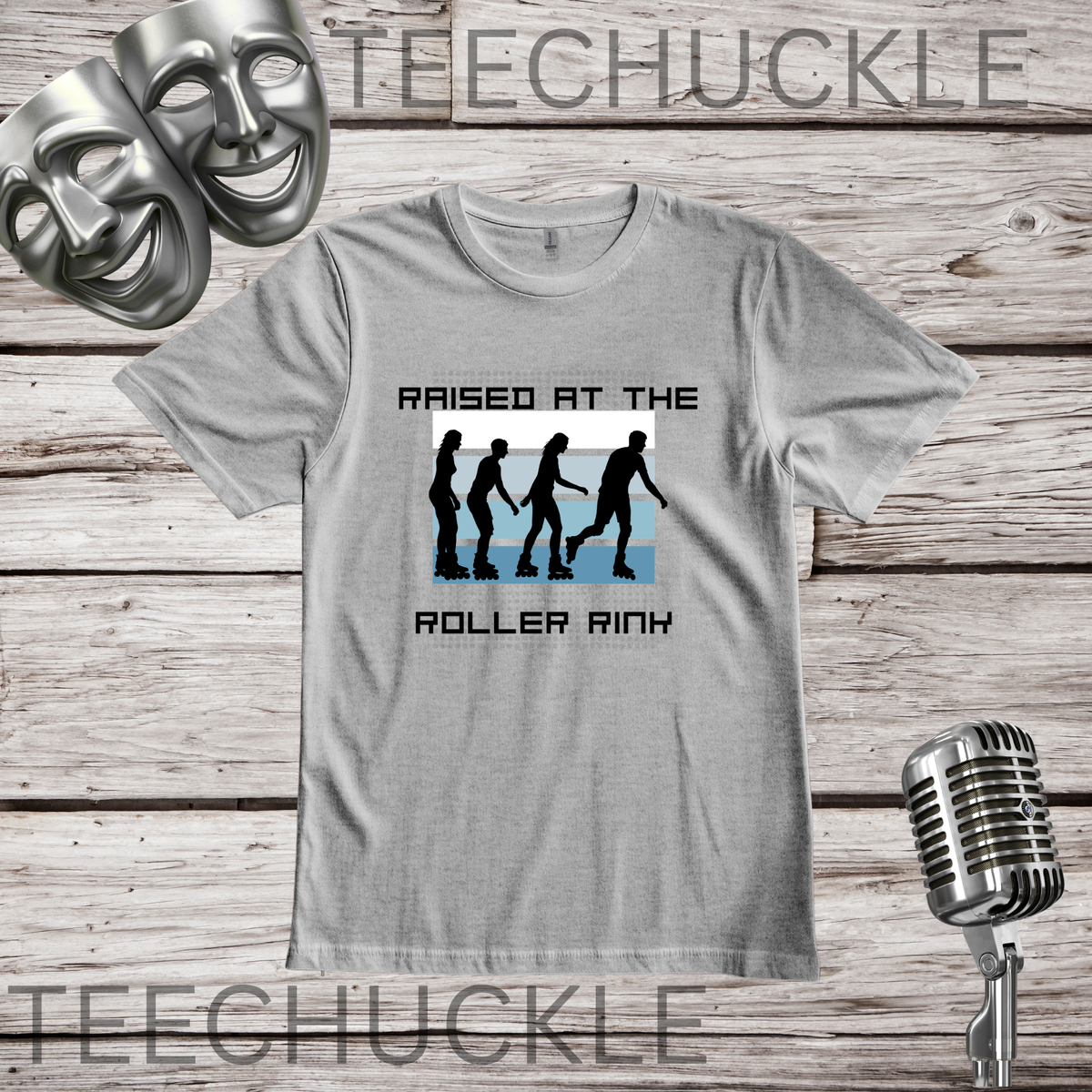 A gray graphic t-shirt displayed on a rustic wood background, featuring a black and blue graphic of silhouettes in roller skaters with the text 'RAISED AT THE ROLLER RINX'. The image includes decorative props like a silver microphone and theatrical masks