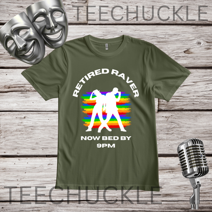 A green graphic t-shirt displayed on a rustic wooden background with vintage props including a silver microphone and theatrical masks. The t-shirt features a white graphic of a person dancing in front of a rainbow-striped sunset, with the text 'RETIRED RAVER NOW BED BY 9PM'.