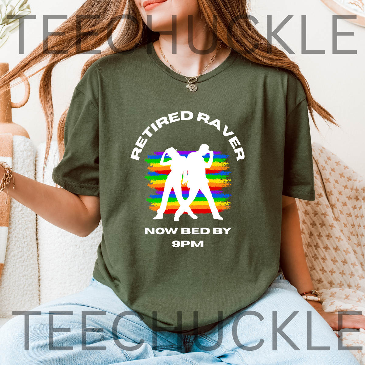 A woman wearing a green graphic t-shirt with a 'Retired Raver Now Bed By 9PM' design featuring white text and two dancing figures over a rainbow stripe background.