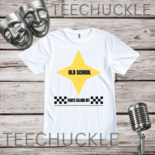 A white short-sleeve graphic T-shirt laid flat on a rustic wood plank background, with two silver comedy masks and a vintage microphone as props. The shirt has a large yellow star graphic with the words 'OLD SCHOOL' in black, plus a black-and-white checkered bar and the phrase 'PARTS FALLING OFF' below.