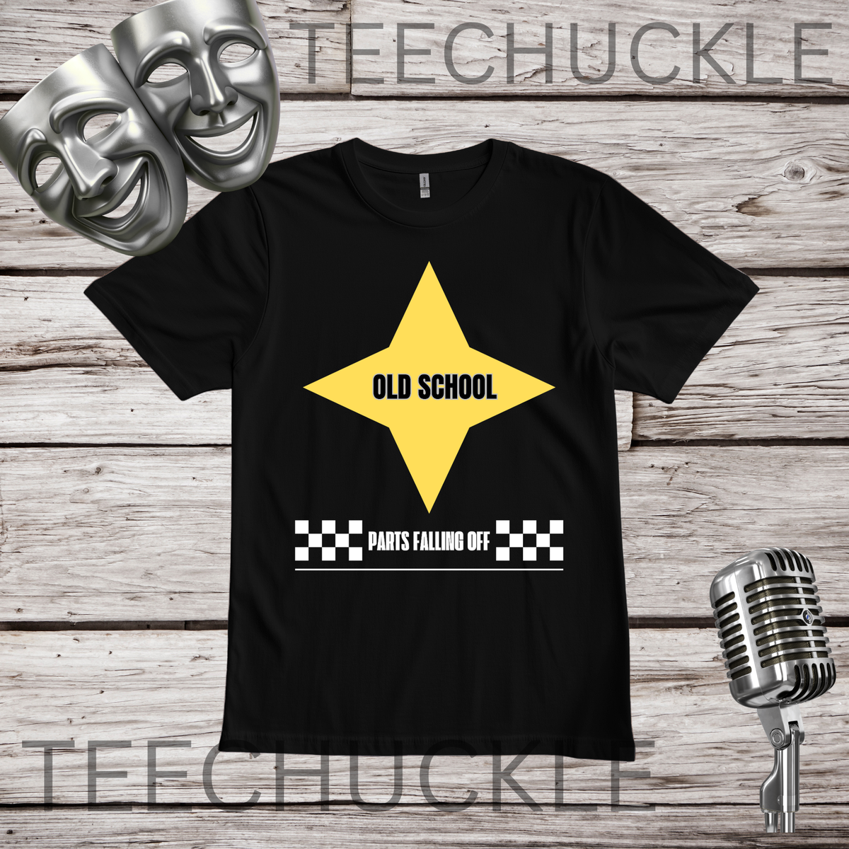 A black short-sleeve graphic T-shirt laid flat on a rustic wood plank background, with a large yellow star graphic and the words 'OLD SCHOOL' and 'PARTS FALLING OFF' printed on the front. Silver theater masks and a vintage microphone are placed around the shirt as styled props.