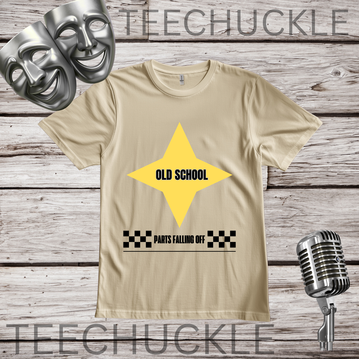 A beige graphic t-shirt displayed on a rustic wood background, featuring a yellow star graphic with the text 'OLD SCHOOL' and 'PARTS FALLING OFF' with a black checkered pattern. The shirt is styled with silver comedy masks