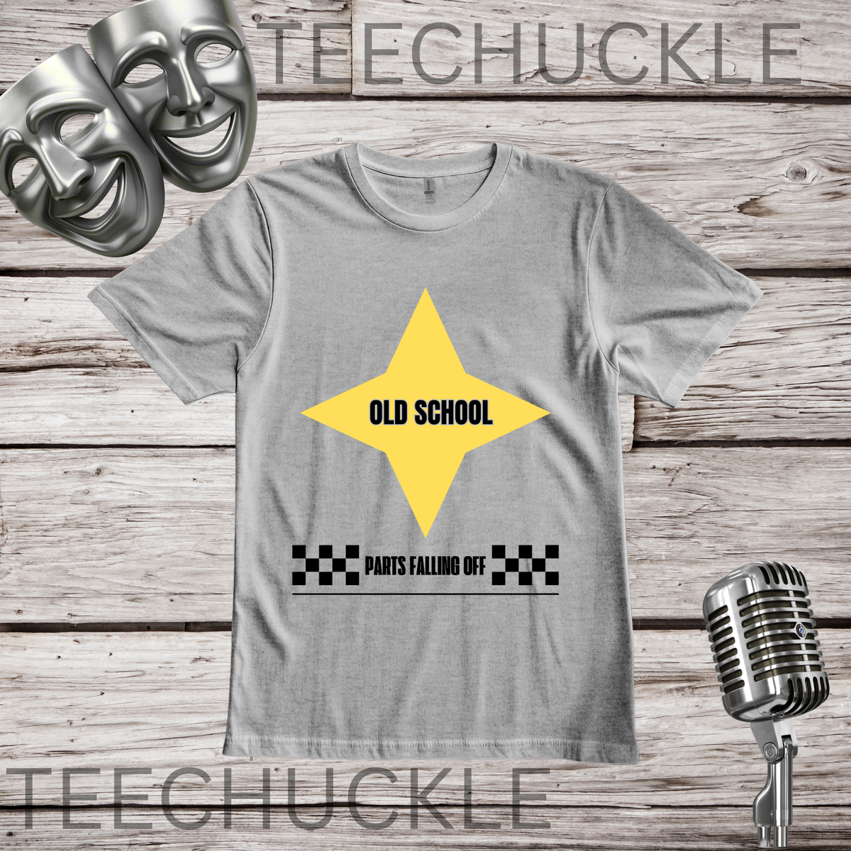 A gray crewneck t-shirt with a yellow star graphic containing the text 'OLD SCHOOL' and a black-and-white checkered bar below reading 'PARTS FALLING OFF'. The shirt is displayed on a rustic wooden background with a vintage microphone, comedy masks.