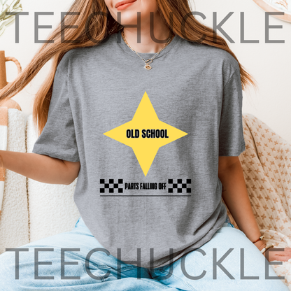 A woman wearing a gray graphic t-shirt with a yellow star and the text 'OLD SCHOOL PANTS FALLING OFF'.