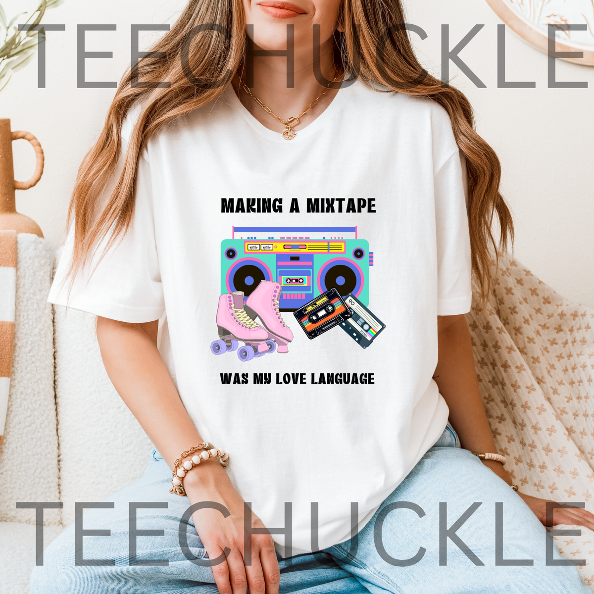 A woman wearing a white graphic t-shirt with a retro 80s boombox, cassette tape, and roller skate print, sitting on a couch. The t-shirt features the text 'MAKING A MIXTAPE WAS MY LOVE LANGUAGE'.