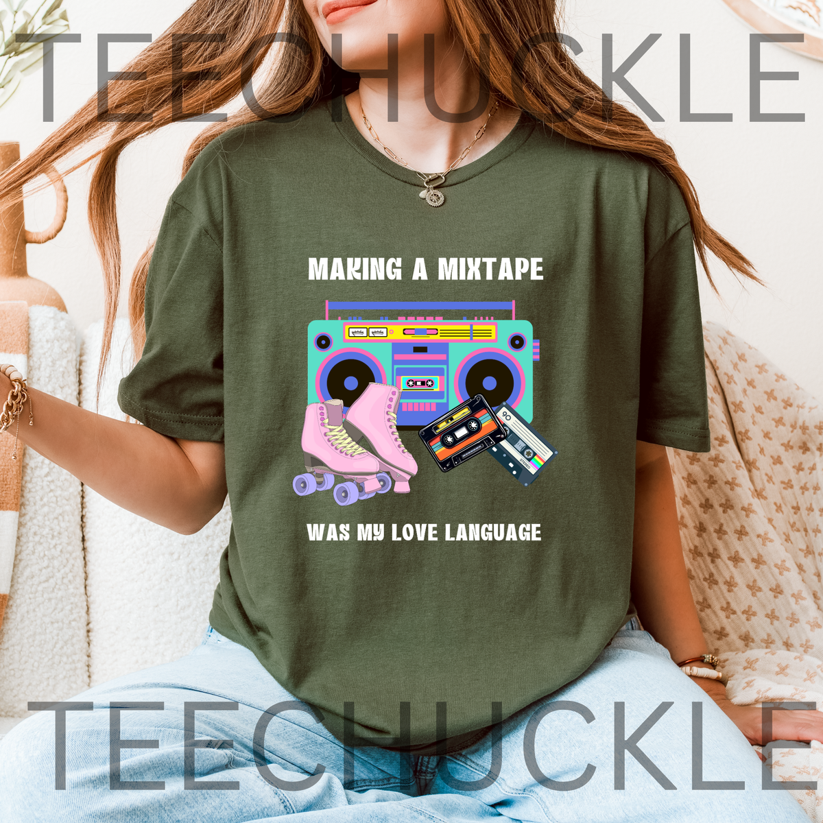 A woman wearing a green graphic t-shirt with a retro boombox, pink roller skate, and cassette tapes design with the text 'MAKING A MIXTAPE WAS MY LOVE LANGUAGE'.