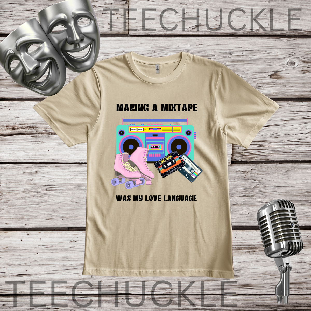 A sand graphic t-shirt displayed on a rustic wood background, featuring a retro cassette tape and boombox design with the text 'MAKING A MIXTAPE WAS MY LOVE LANGUAGE'. The shirt is styled with silver theater masks, a vintage microphone.