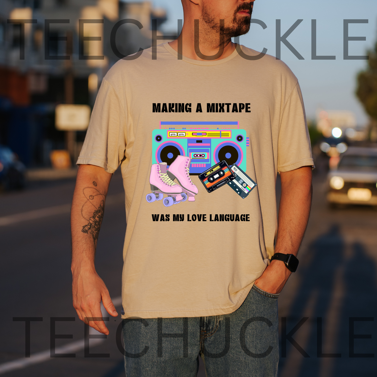 A man wearing a sand graphic t-shirt with a retro 80s boombox and cassette tape design, standing on a blurred street at sunset. The t-shirt features the text 'MAKING A MIXTAPE WAS MY LOVE LANGUAGE' and a colorful graphic of a boombox, cassette, and pink roller skate.