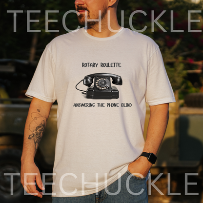 A man wearing a white graphic t-shirt with a black rotary telephone print and the text 'ROTARY ROULETTE' and 'ANSWERING THE PHONE BLIND'. The background is a blurred outdoor setting