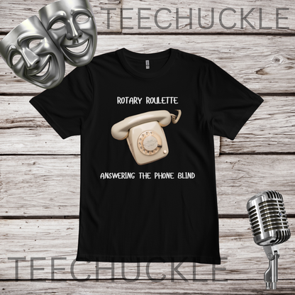A black short-sleeve graphic t-shirt featuring a retro cream rotary telephone and the text 'ROTARY ROULETTE' and 'ANSWERING THE PHONE BLIND'. The shirt is displayed on a rustic wood background with silver theater masks, a vintage microphone.