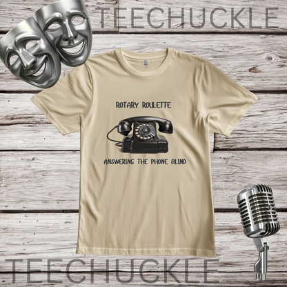 A sand graphic t-shirt featuring a black rotary telephone and the text 'ROTARY ROULETTE' and 'ANSWERING THE PHONE BLIND'. The t-shirt is displayed on a rustic wood background with silver comedy and microphone masks, a vintage microphone.