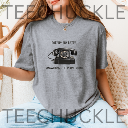 A woman wearing a gray graphic t-shirt with a black rotary telephone design and the text 'ROTARY ROULETTE' and 'ANSWERING THE PHONE BLIND'.