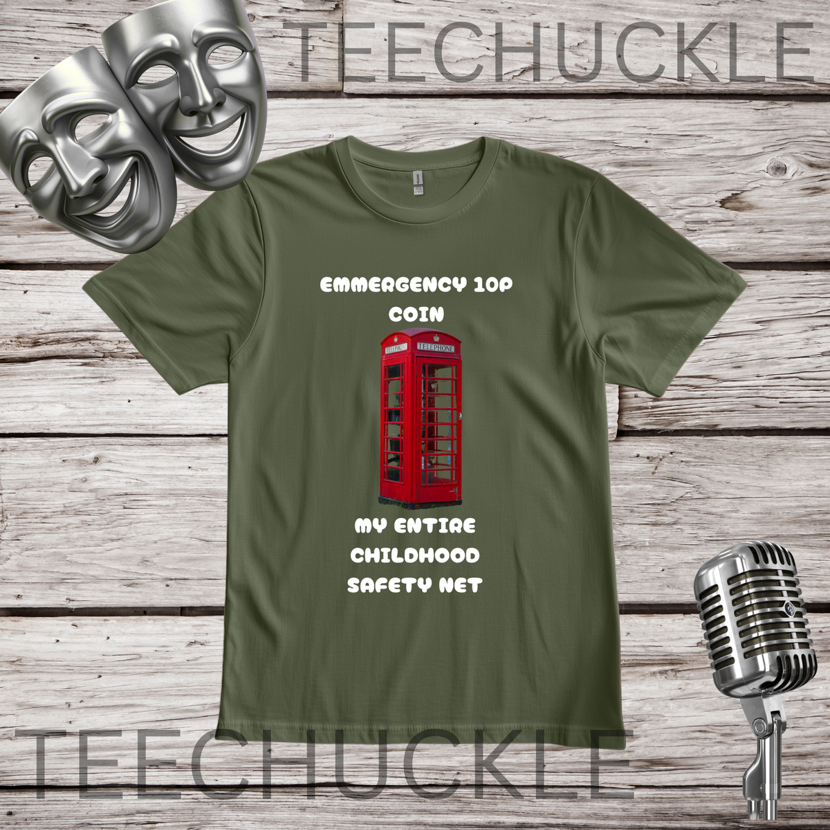 A green graphic t-shirt displayed on a rustic wooden background, featuring a red telephone booth graphic and the text 'EMERGENCY 10P COIN MY ENTIRE CHILDHOOD SAFETY NET'. The shirt is styled with silver theater masks, a vintage microphone.
