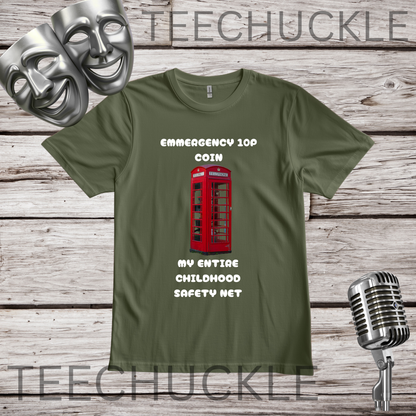 A green graphic t-shirt displayed on a rustic wooden background, featuring a red telephone booth graphic and the text 'EMERGENCY 10P COIN MY ENTIRE CHILDHOOD SAFETY NET'. The shirt is styled with silver theater masks, a vintage microphone.