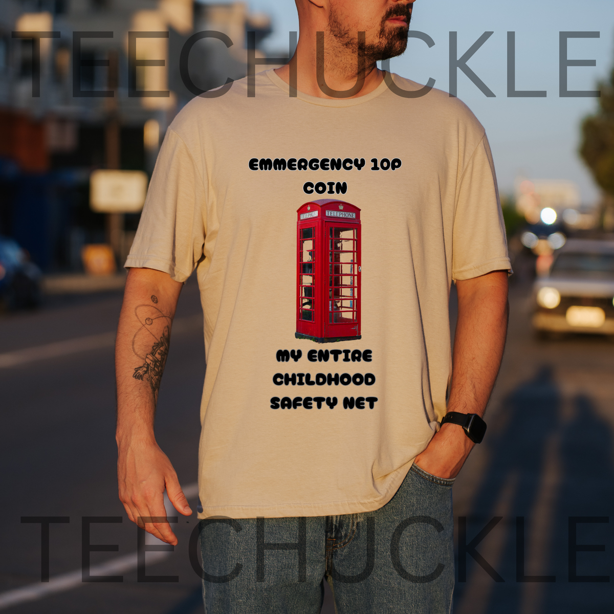 A man wearing a sand graphic t-shirt with a red telephone booth print and the text 'EMERGENCY 100 COIN MY ENTIRE CHILDHOOD SAFETY NET'.