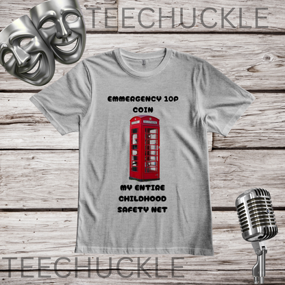 A gray crewneck t-shirt featuring a graphic of a red telephone booth with the text 'EMERGENCY 10P COIN MY ENTIRE CHILDHOOD SAFETY NET' printed on the front. The shirt is displayed on a rustic wood background with a vintage microphone, comedy masks.