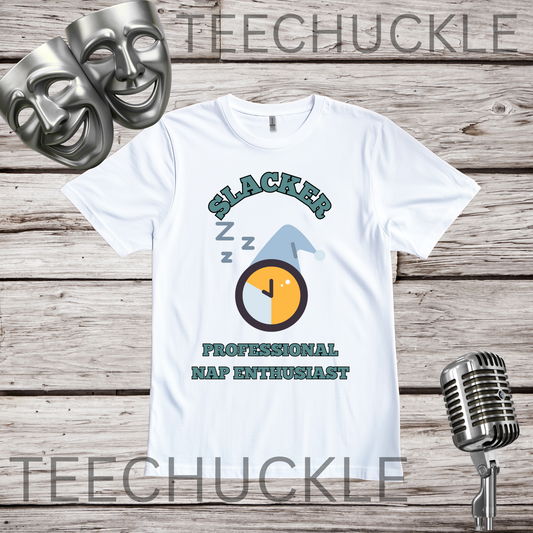 A white graphic t-shirt displayed flat on a rustic wood background, featuring a 'Slacker Professional Nap Enthusiast' design with a sleeping clock and blue nap icon. The shirt is flanked by two silver theatrical masks on the left and a vintage-style microphone on the right