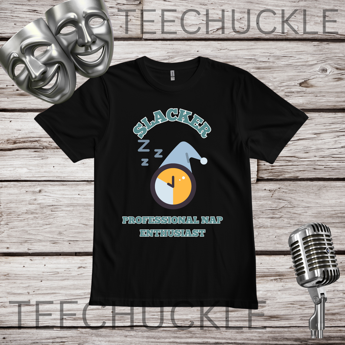 A black short-sleeve graphic t-shirt displayed on a rustic wood background with decorative props including two silver theater masks, a vintage microphone. The graphic features the word 'SLACKER' in a light teal arched font above a clock illustration with 'Z' sleep sounds and a blue sleeping hat, followed by 'PROFESSIONAL NAP ENTHUSIAST' in light teal.