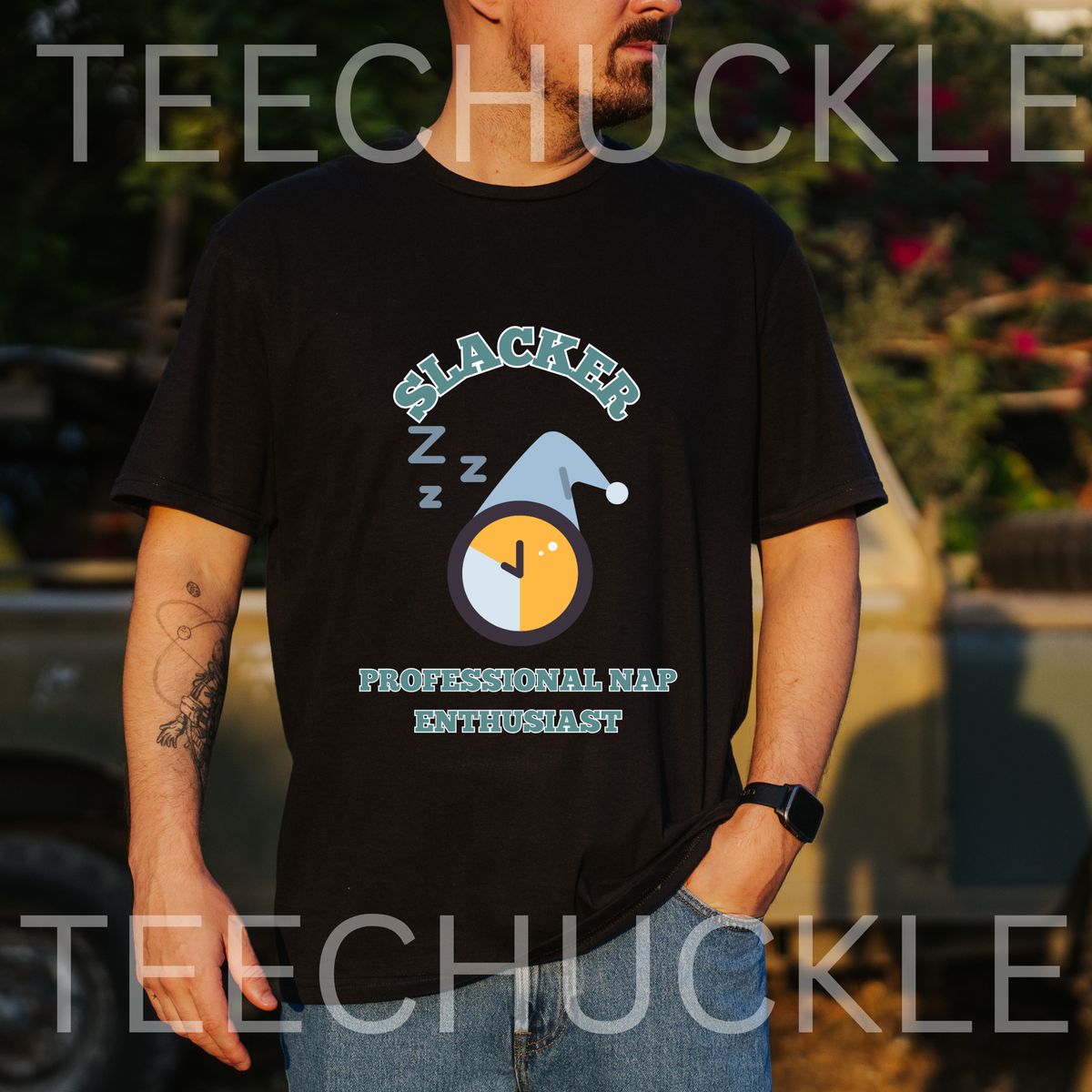 A man wearing a black graphic t-shirt with a 'Slacker Professional Nap Enthusiast' design, standing outdoors in front of a blurred vehicle.