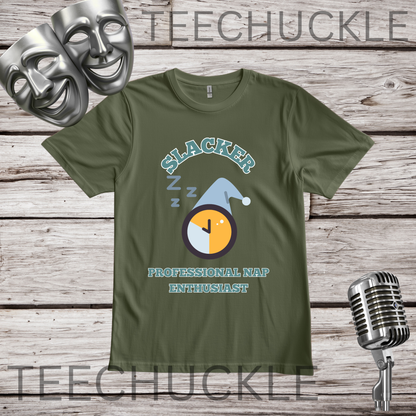 A green graphic t-shirt displayed on a rustic wood background, featuring a 'Slacker Professional Nap Enthusiast' design with a sleeping clock and hat. The image includes decorative props like a silver comedy mask, a vintage microphone