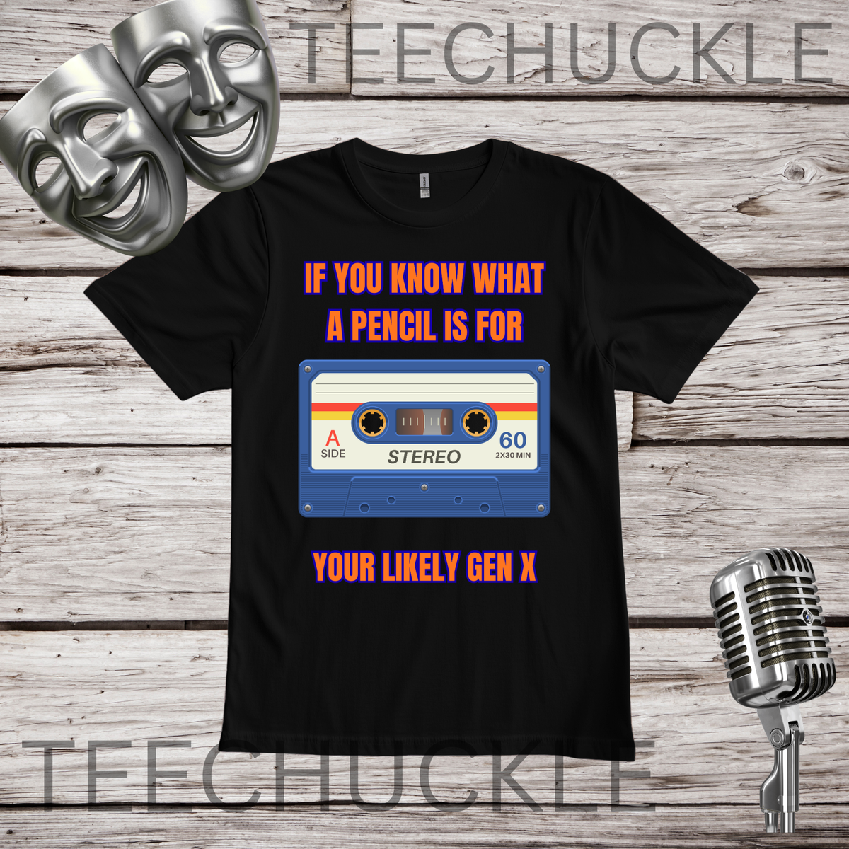 A black short-sleeve graphic t-shirt displayed flat on a rustic wood background, featuring a cassette tape graphic with the text "IF YOU KNOW WHAT A PENCIL IS FOR YOU'RE LIKELY GEN X". The image includes decorative props like two silver theater masks, a vintage microphone,.